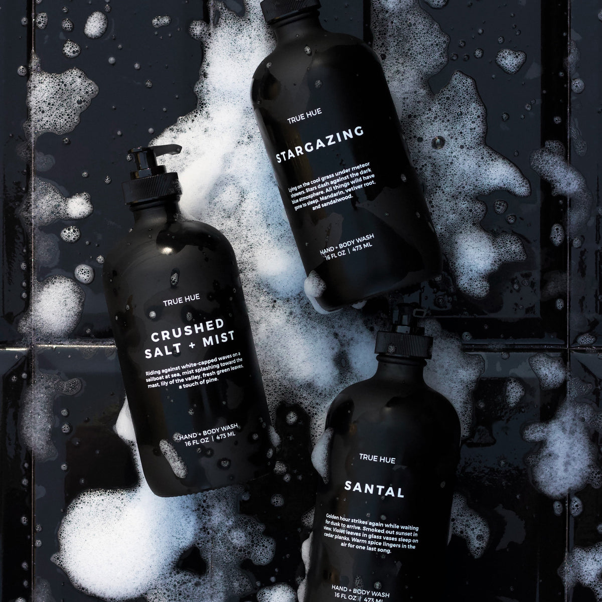 3 black bottles of hand soap laying on a soapy, black tile background.