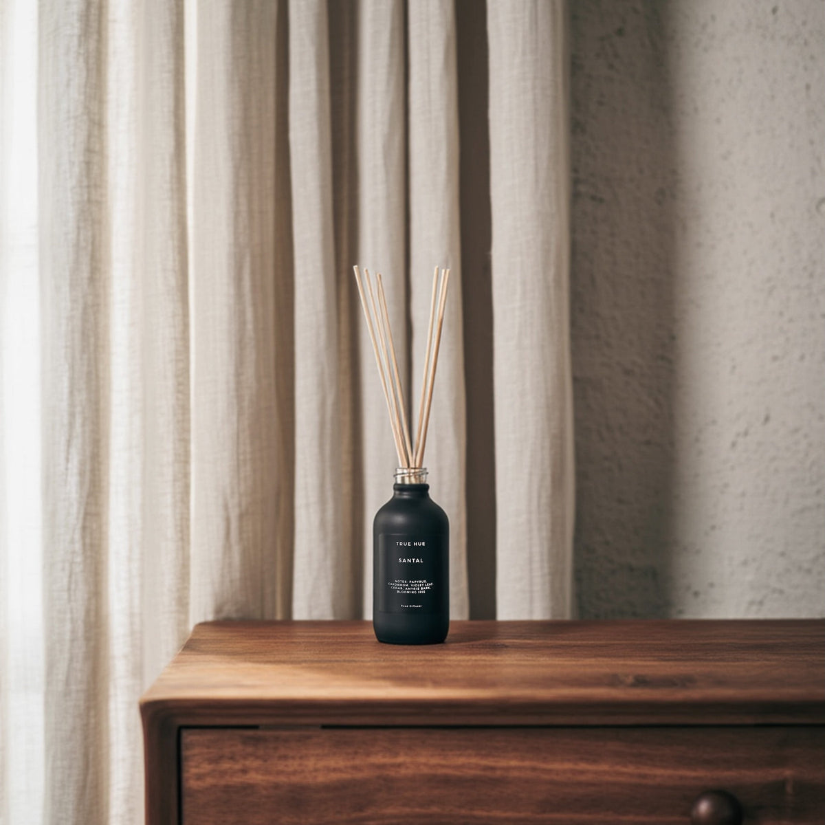 Santal Reed Diffuser sitting on a wooden dresser with beige curtains in the background.