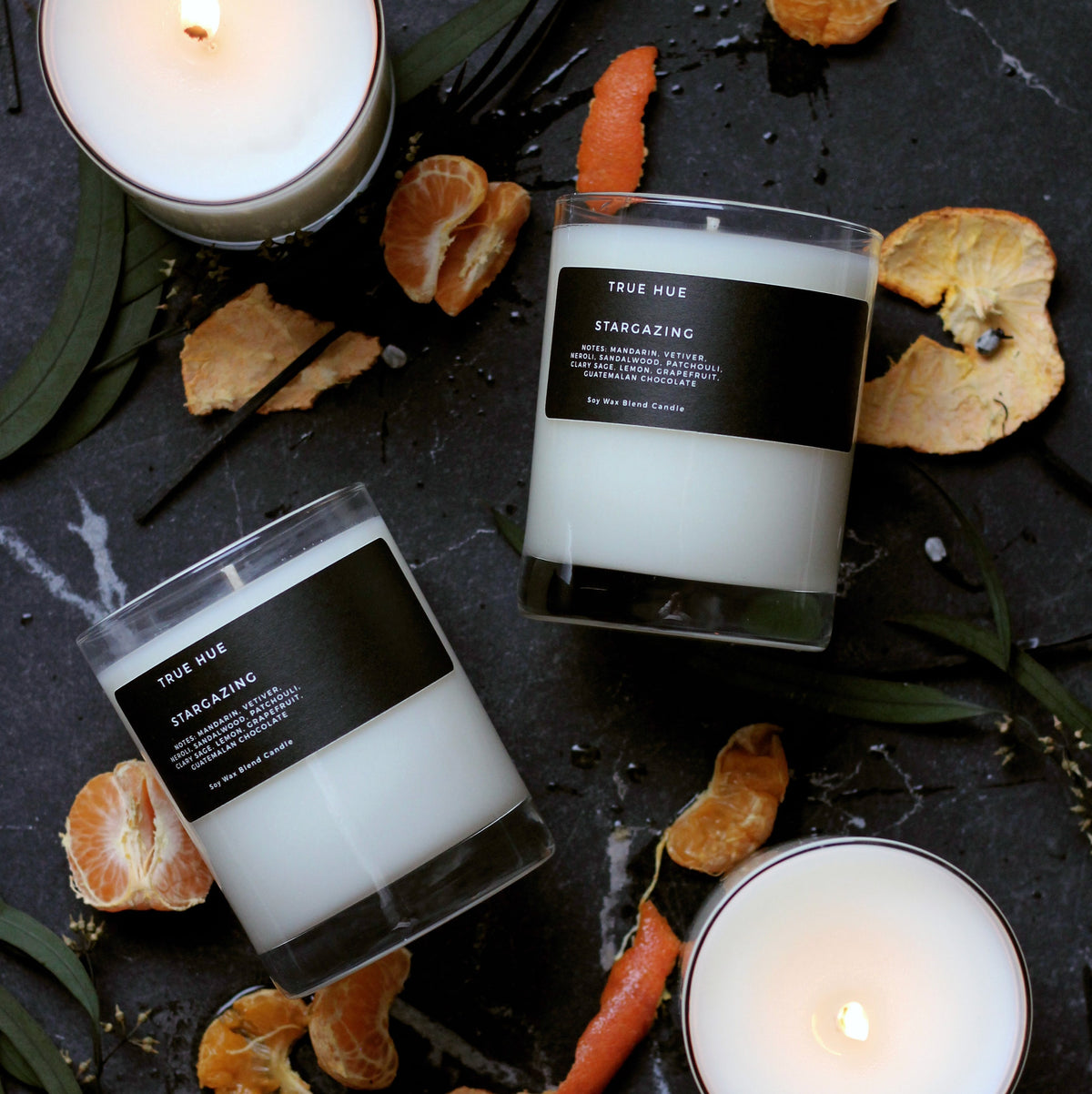 large stargazing candles against a black marble background with mandarin oranges and leaves.