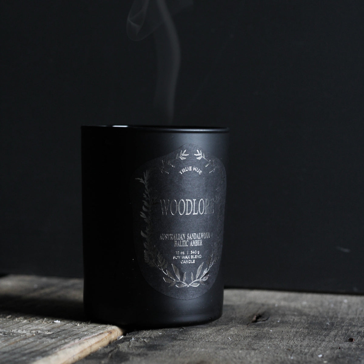 Woodlore Candle on a wooden table with smoke coming off of the extinguished candle.