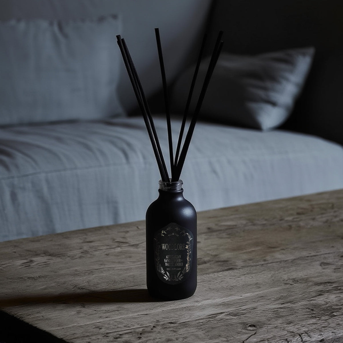 Woodlore Reed Diffuser sitting on a wooden coffee table with a moody gray background.