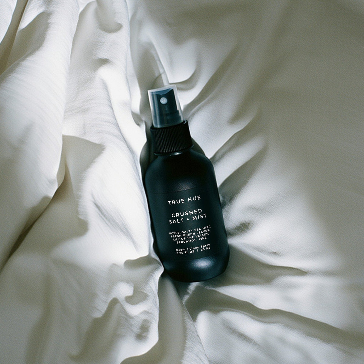 Crushed Salt + Mist Room / Linen Spray bottle laying on a white bed sheet.