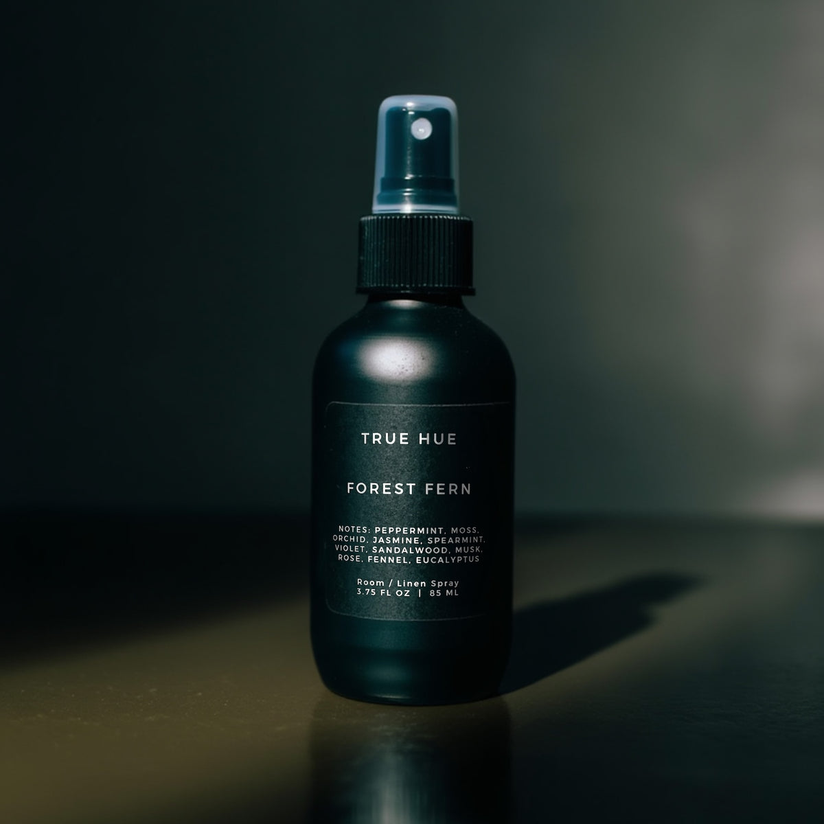 Black spray bottle labeled 'True Hue Forest Fern' on a dark background