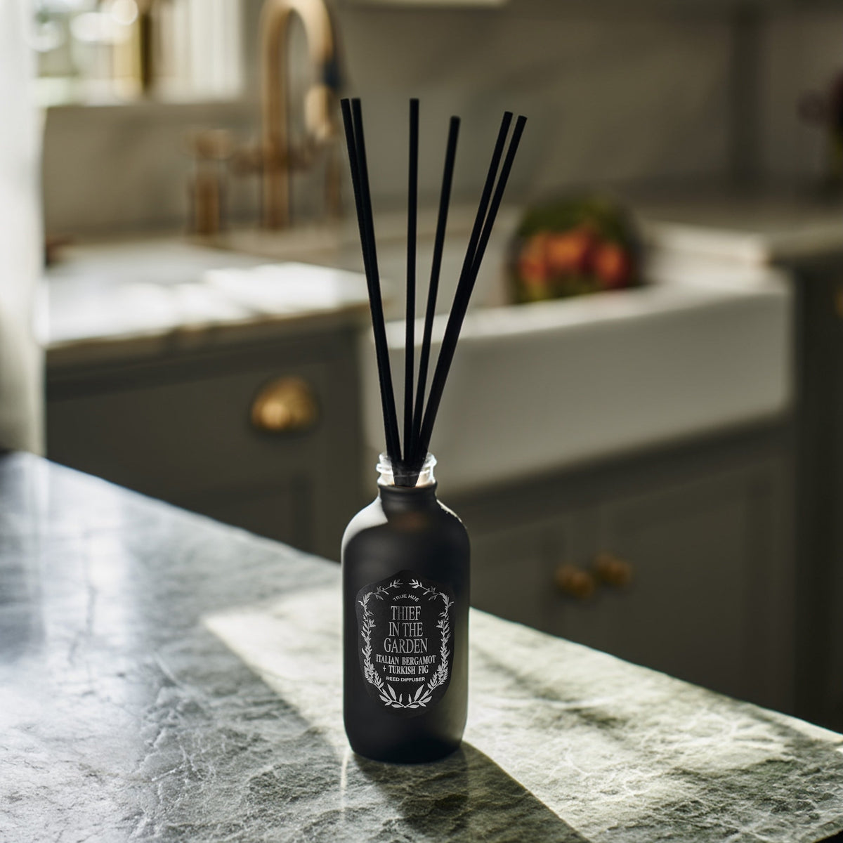 Thief In The Garden Reed Diffuser sitting on a green marble kitchen countertop.