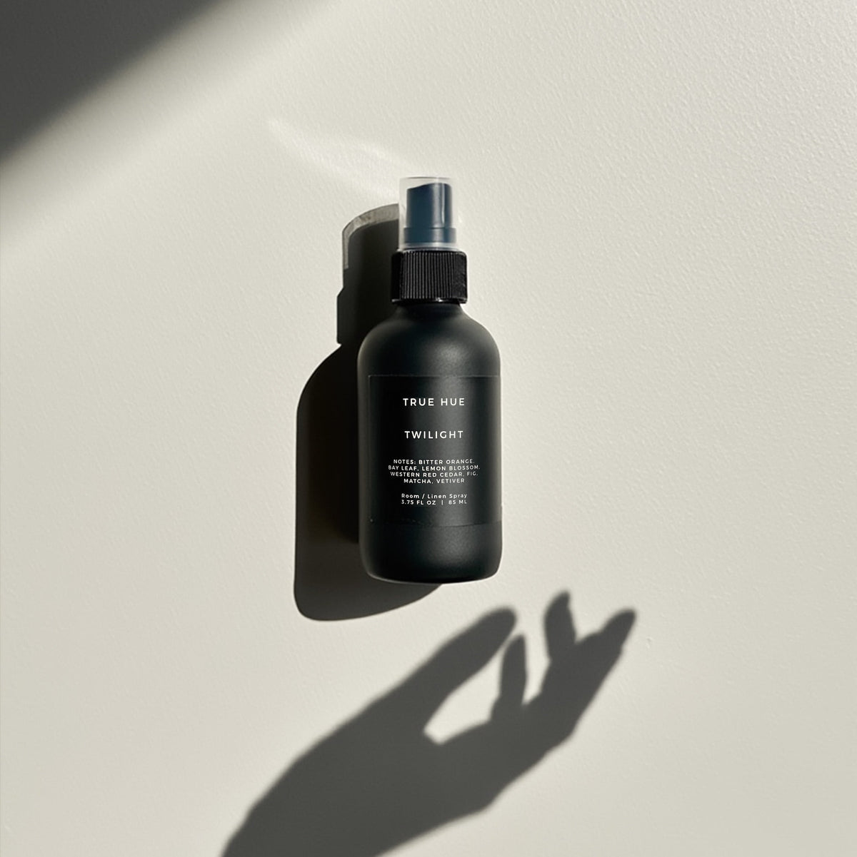 bottle of twilight room spray on a light gray background with a shadow of a hand reaching for the bottle.